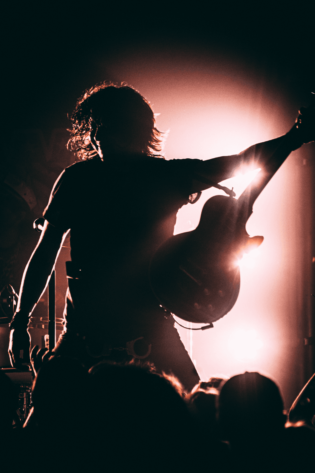 A guitarist silhouetted against warm stage lights, arm raised to the crowd