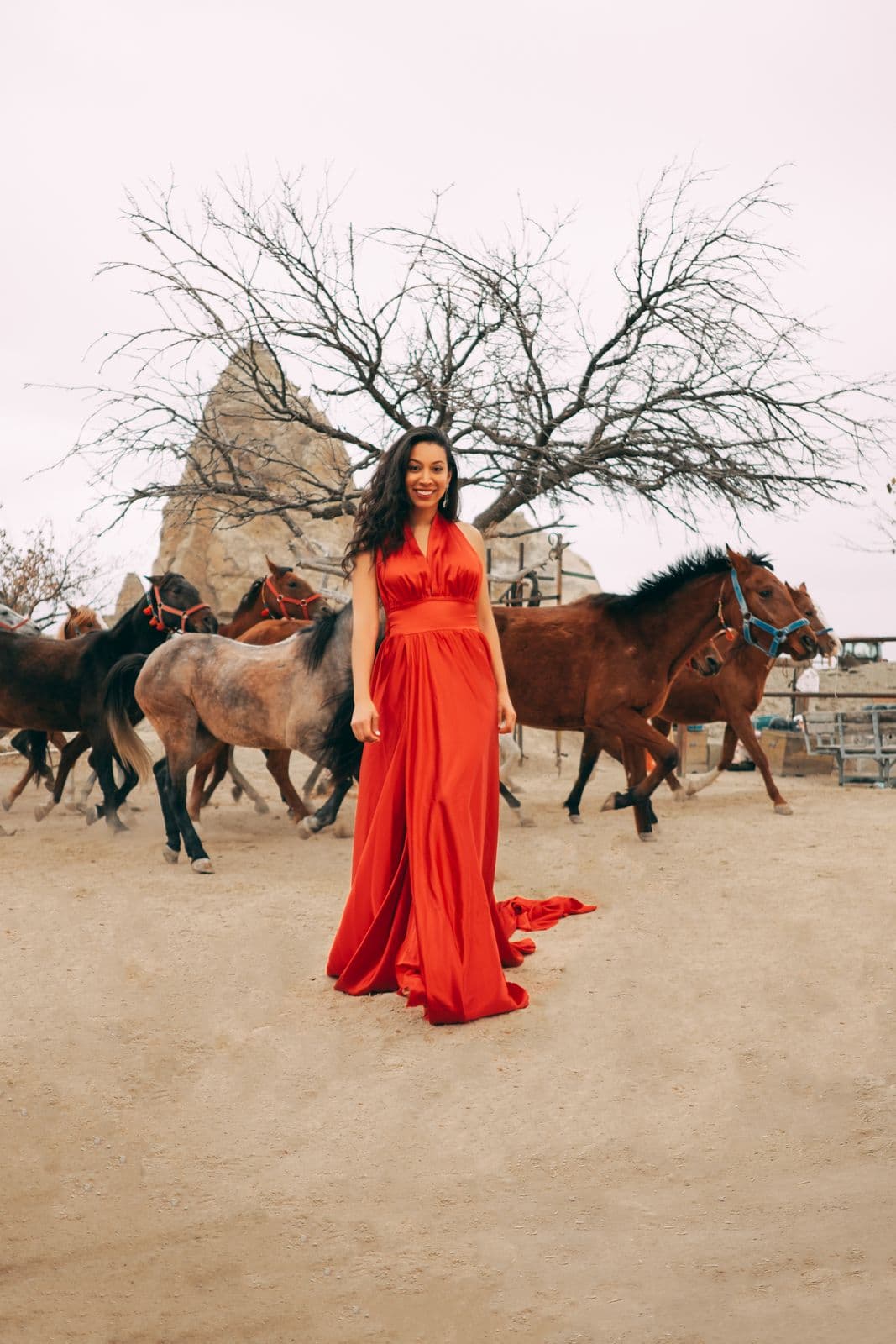 A woman in a flowing red dress standing among a herd of horses
